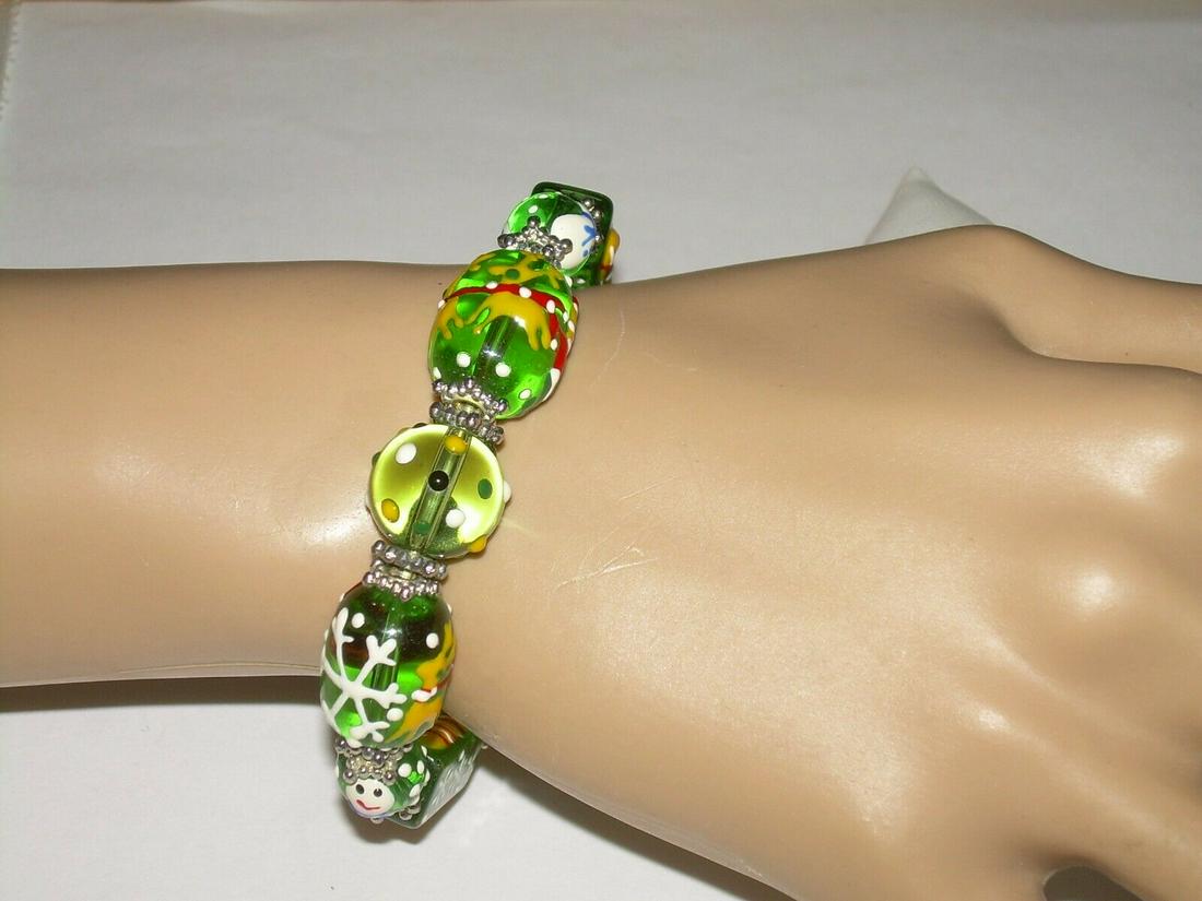 Vintage Bead Stretch Bracelet - XMAS Theme with: Vintage asscented green and oval faceted beads make - up this Christmas themed stretch bracelet. The beads depict a variety of items for the holiday. There are snowmen, stockings, reindeer, candles, c