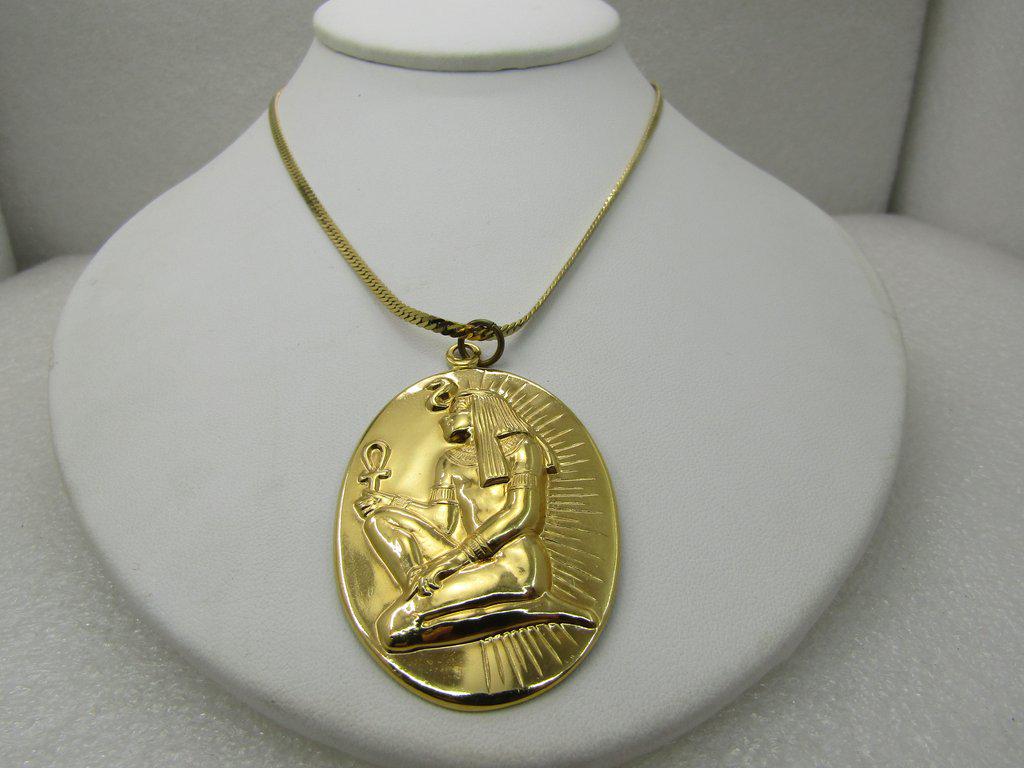 Vintage Egyptian With Ankh Pendant on Monet, 24": Vintage Egyptian With Ankh Pendant on Monet, 24" Herringbone Chain. Gold Tone. The pedant is a pressed Egyptian scene, kneeling figure with asp holding ankh. It is 2.25" long and 1.25 wide. The chain 