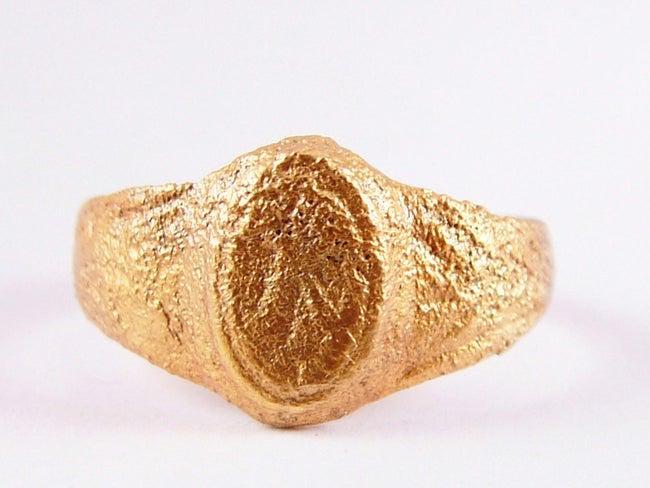 MEDIEVAL WOMAN'S FASHION RING SIZE 9 3/4: C.900-1300 AD. Good wearable size 9 3/4. Rounded band 4.1mm width with flared floral decorated shoulders. Raised oval bezel with floral motif cut in. This ring, by its quality, would have distinguishe