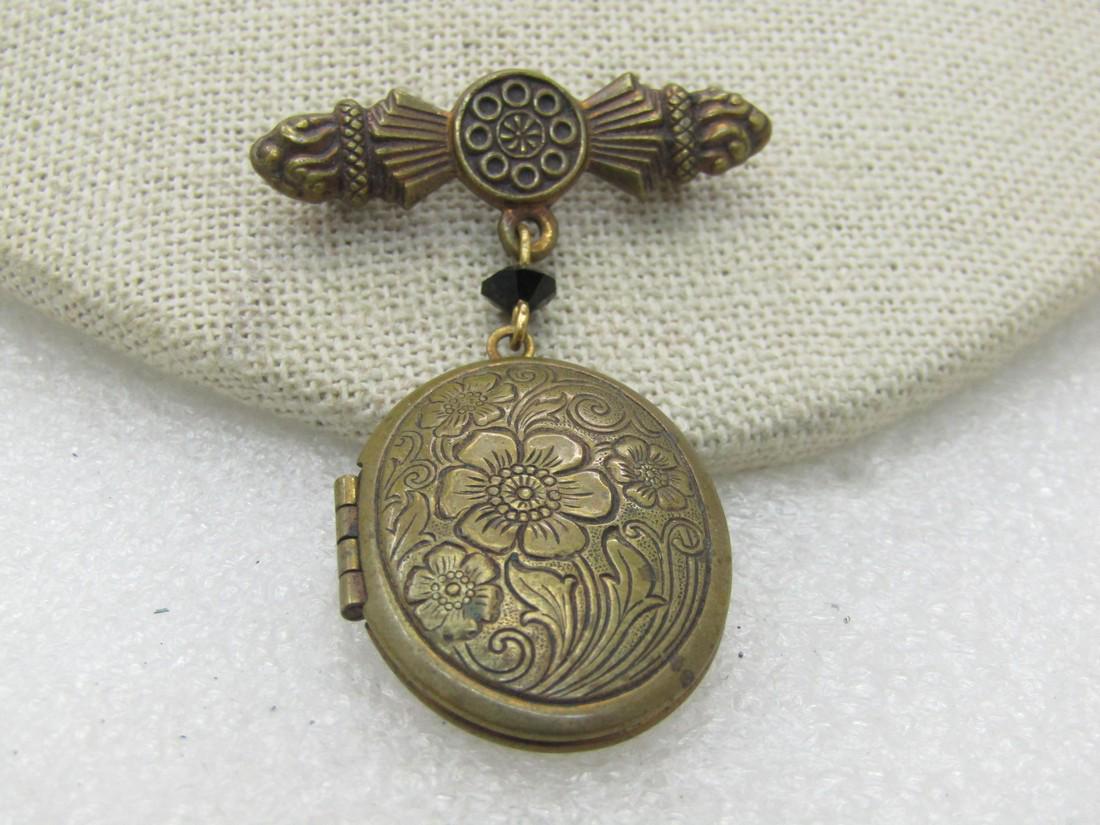 Vintage 1930's Locket Brooch, Floral, 2": Vintage 1930's Locket Brooch, Floral, 2" long, 1" wide. Brass with a Victorian themed bar brooch from which the floral hinged locket hangs. It is a black facete glass bead between the locket and bar b