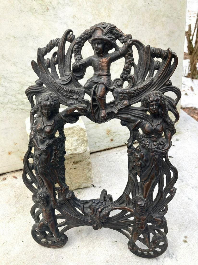 C1900 elaborate cast iron free standing frame: Title: C1900 elaborate cast iron free standing frame Dimensions: Inside measures 4" x 5 3/4". Outside measures 9 1/2" x 14". Provenance/Additional Info: An assortment of figures including cherubs. Mak