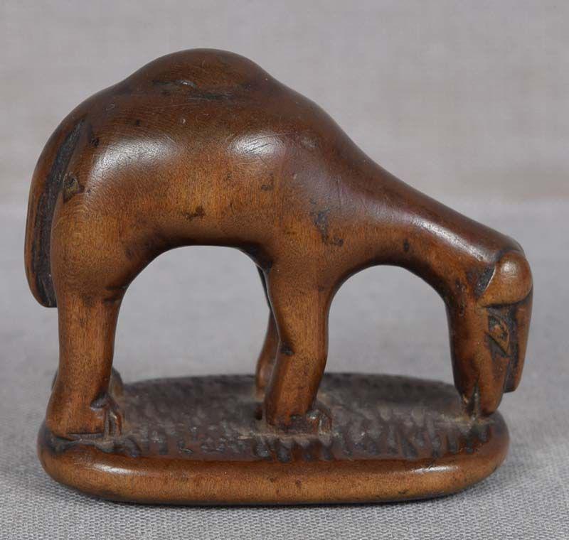 18c netsuke GRAZING CAMEL: 18th century boxwood netsuke of a grazing camel. Actually unusual animal in netsuke, very nicely carved, good rendition of its posture and hump. The face is rather fantastical - the carver must have n