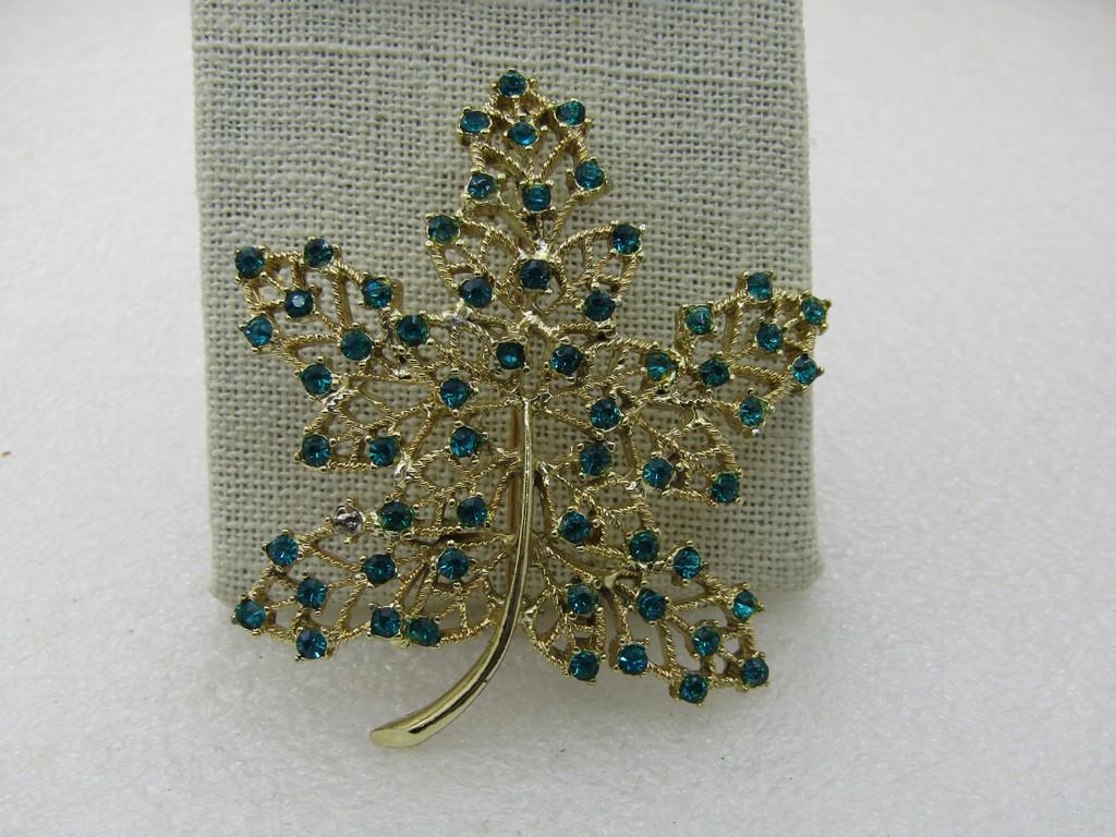 Vintage Green Rhinestone Maple Leaf Brooch, 2.75", Gold: Vintage Green Rhinestone Maple Leaf Brooch, 2.75" by 2.5", Gold Tone, 1960's. Filigree leaf with open areas of textured gold tone metal and a smooth stem. Green rhinestones dot the leaf. One was missi
