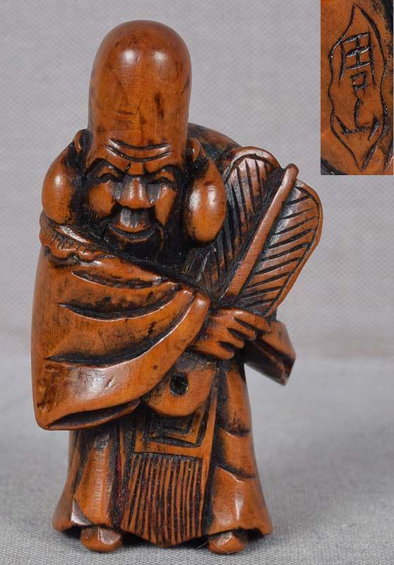 19c netsuke God FUKUROKUJU by NAGAMACHI SHUZAN: 19th century boxwood netsuke of Fukurokuju with his characteristic elongated head wearing a longsleeved robe and holding a fan in his hand. He is one of the Seven Gods of Good Fortune, his name consis