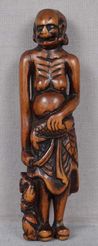 18c netsuke South Seas ISLANDER with fish 94mm: 18th century good size wooden netsuke of a monstrously tall South Seas islander wearing a leaf skirt and holding a fish in one hand, with a man in Chinese robe hardly reaching a knee level of the gian