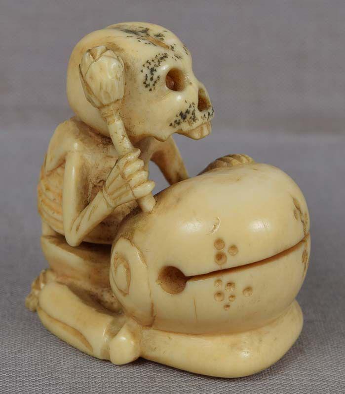 19c marine netsuke Priest DANKA SKELETON with gong &: 19th century marine material netsuke of a skeleton holding a lotus stem with bud in his hand kneeling next to mokugyo (Buddhist temple gong). The subject is a ghost of a late Buddhist priest Danka. Wo