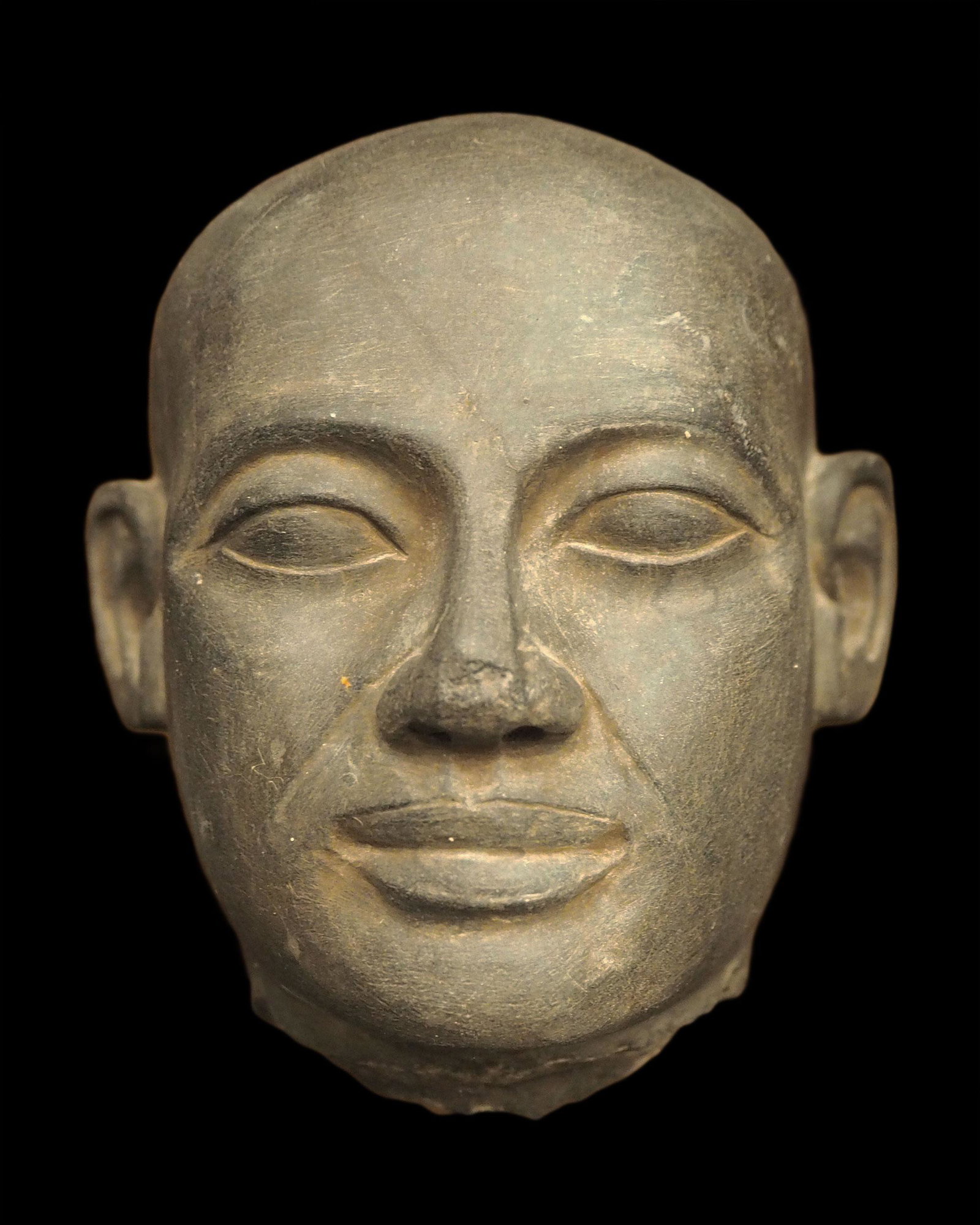 Egyptian schist head of a priest: Title: Egyptian schist head of a priest Description: Schist head of a priest with a creased forehead and shaven egg-shaped skull, his oval face with almond-shaped eyes. Priests played an important rol