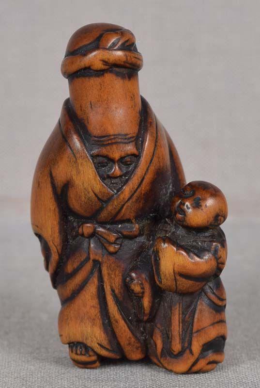 19c netsuke LUCKY GOD FUKUROKUJU with boy by: 19th century boxwood netsuke of Fukurokuju with his characteristic elongated head with a sweat band tied around its top as it is half way hidden within a long sleeved robe, and an attendant boy lookin