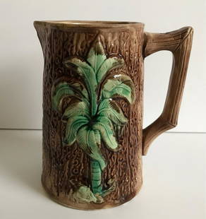 Majolica Pitcher: Nice Victorian Majolica pitcher decorated with a palm tree. Stands 6.5" tall. Top edge is smooth to the touch, but appears to have a little roughness (see photos). Otherwise, condition is good and