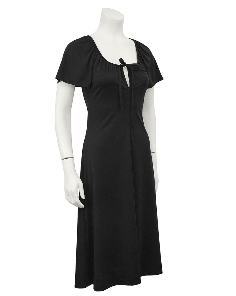 Clovis Ruffin: Black Keyhole Dress: 1970s Clovis Ruffin "Ruffinwear" polyester black jersey dress with keyhole tie at neckline. The dress has a gathered neckline with cape style short sleeves and a tie at the top of the bust that create