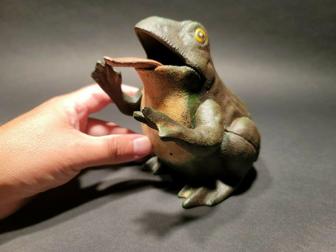 Cast Iron Frog Mechanical Coin Bank: 5 3/4" Tall 5" Wide Great reproduction folk art cast iron mechanical coin bank. This piece was made to look just like an antique, but is actually new. By pressing the arm of the frog the tongue will r