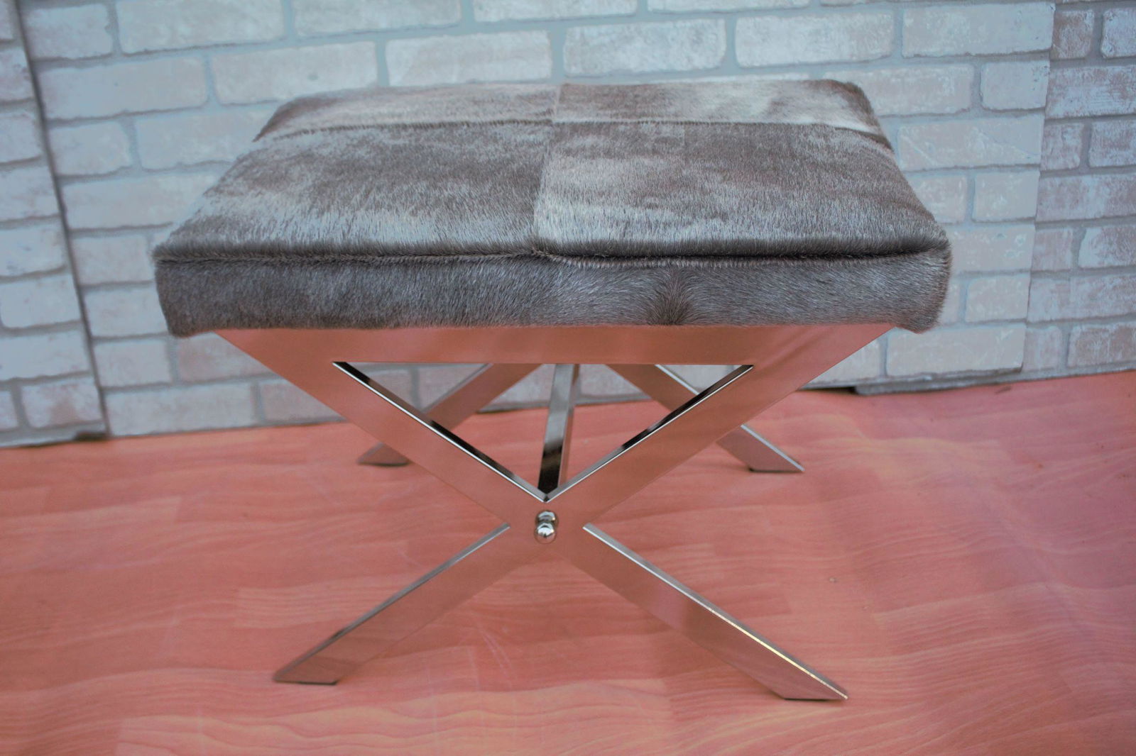 Modern Tangent Chrome X Design Stool with Cow Hide Top: Materials: chrome, cow hide, animal skin, metal Description Modern Tangent Chrome Flat Bar X Design Base Stool with Gray Cow Hide Top Circa 2019 H 18” W 23” D 17” Seat H 18” Gr