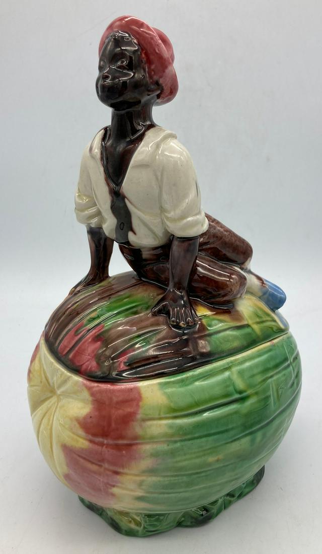 TOBACCO JAR MAJOLICA BLACK AMERICANA BOY FIGURE ON WATERMELON - HUMIDOR: Title: TOBACCO JAR MAJOLICA BLACK AMERICANA BOY FIGURE ON WATERMELON - HUMIDOR Date/Period: UNKNOWN Dimension: APPROX 9.75" TALL X 5.5 LONG Material: ceramic Additional Information: TOBACCO JAR MAJOLI
