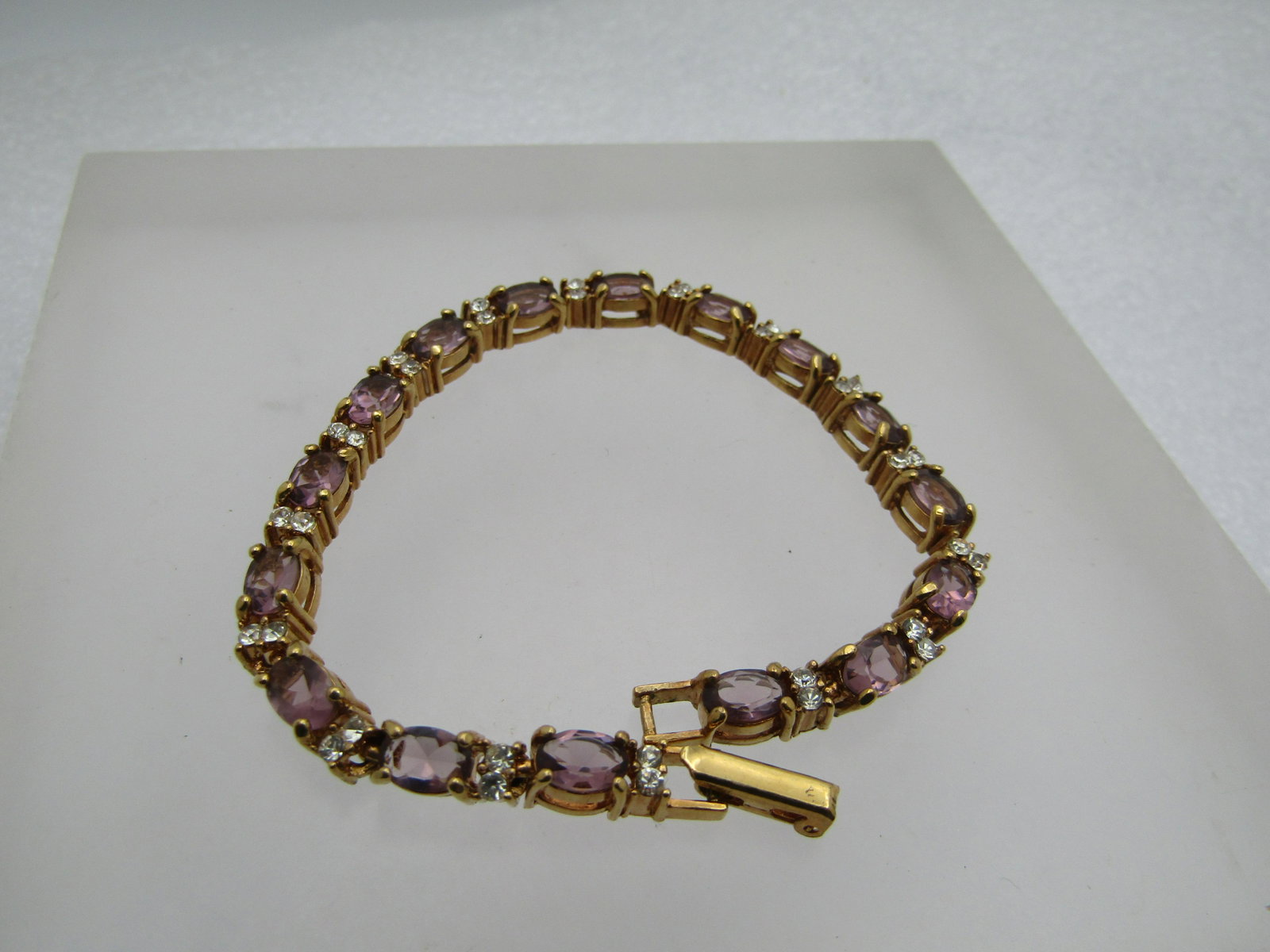Simulated Amethyst Diamond Tennis Bracelet, 7", Signed Avon: Simulated Amethyst Diamond Tennis Bracelet, 7", Signed Avon. Gold tone and appx. 4.5mm wide. Flip clasp. The stones are a purple glass that are appx. 5.5mm by 4mm. There are two appx. 2.5mm round clea