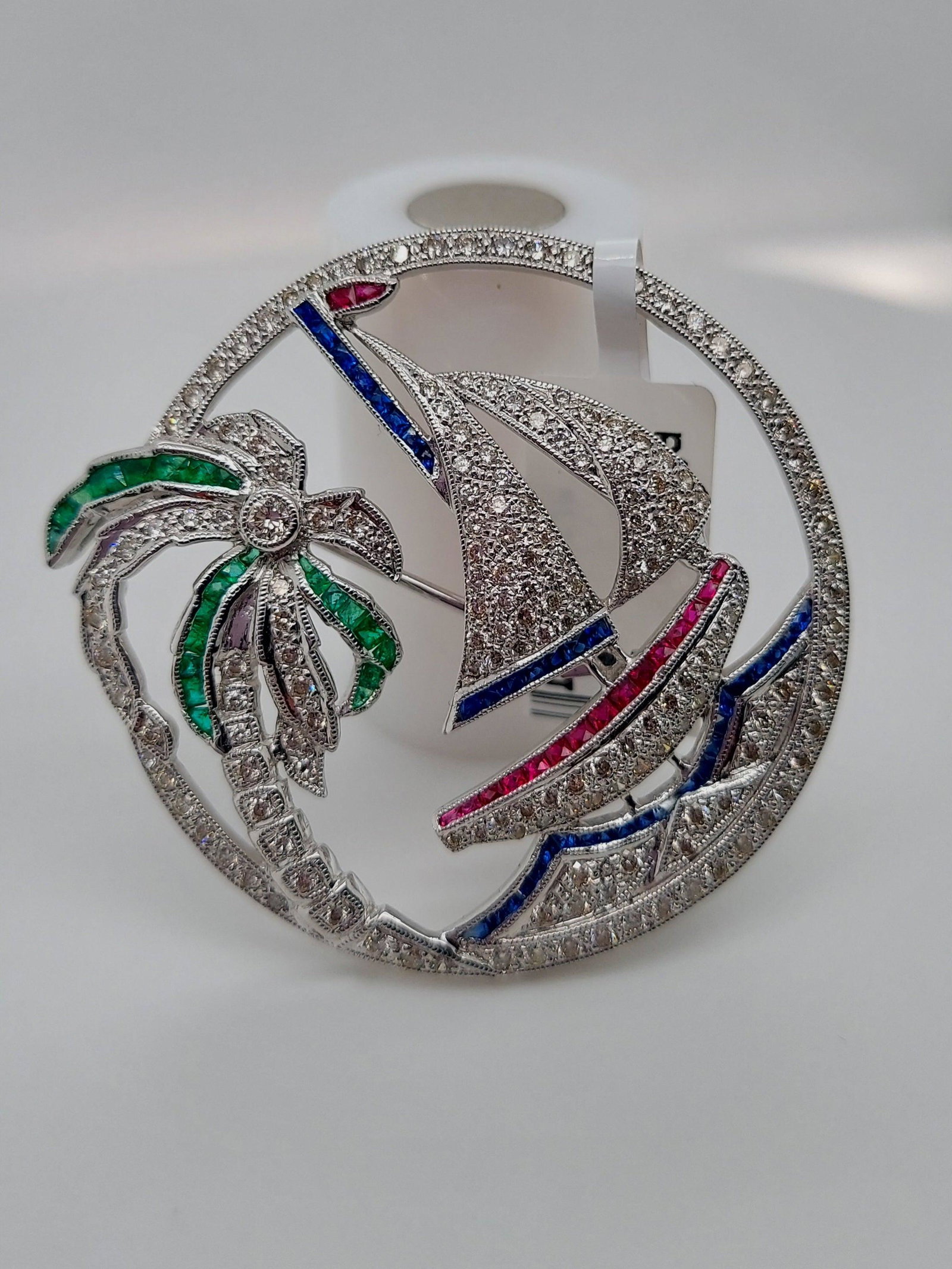 DIAMOND AND MULTI GEM SAIL BOAT BROOCH: Diamond and Multi Gem Sail Boat Brooch Stone: Natural Diamond, Sapphires, Rubys and Emeralds Metal: 18K White Gold Diamond Color: E Diamond Clarity: VS1 Length: 1.5 Inches in Diameter Weight: 14.2 gra