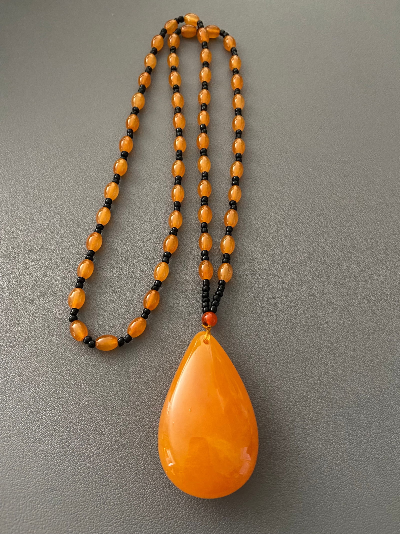 Amber Bakelite Hand Carved Large water drop Pendant with Beaded Chain: Amber Bakelite was popular in the early to mid-20th century for its versatility and durability. It was often used to create jewelry and decorative objects. Hand-carved Bakelite pieces, including penda