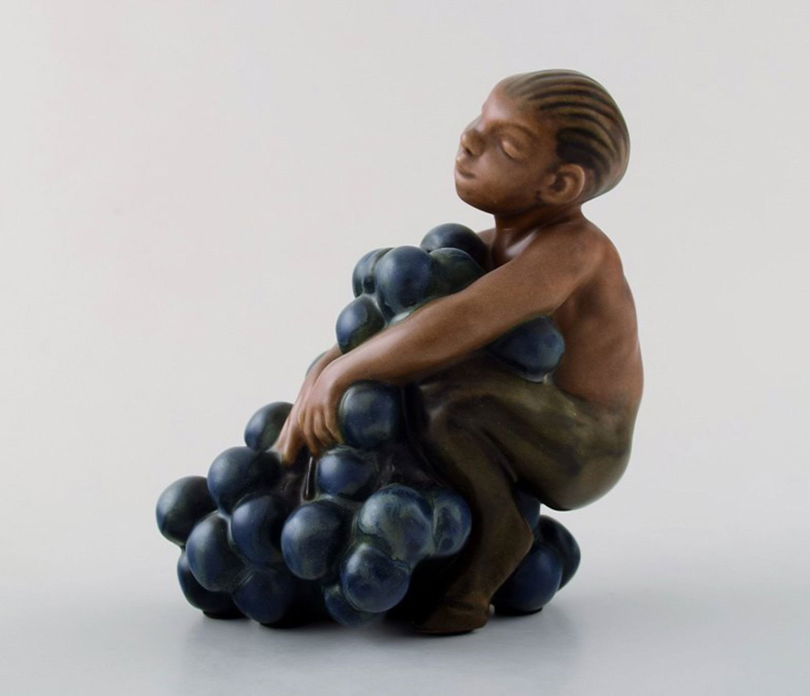 Bing & Grondahl stoneware figurine of small bacchus with bunch of grapes by Kai Nielsen. Model: Title: Bing & Grondahl stoneware figurine of small bacchus with bunch of grapes by Kai Nielsen. Model number 4027. From the series 'Grape Harvesting'. Description: Bing & Grondahl stoneware figurine o