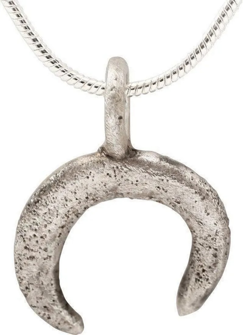VIKING LUNAR PENDANT, 9TH-10TH CENT. AD: About 5/8" height plus the suspension loop. Crescent form with the ends tapering sharply from the swelled middle. As expert navigators, the constellations signified mystery and power to Vikings. The M