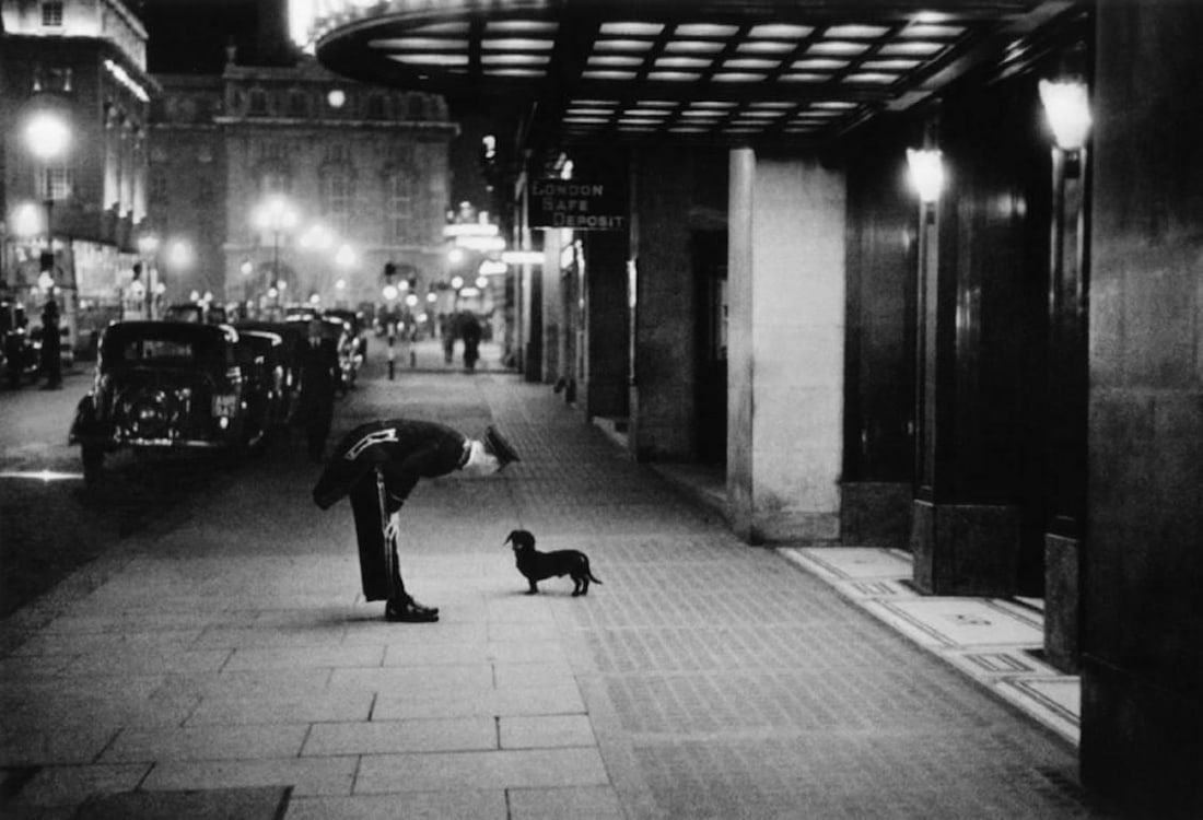 Commissionaire’s Dog' Limited Edition Silver Gelatin Print 1938 (printed later): Commissionaire’s Dog' Kurt Hutton, 1938 A hotel commissionaire talking to a small dachshund dog in Piccadilly Circus, London, 1938. A beautiful image of a commissionaire dressed in uniform, bend