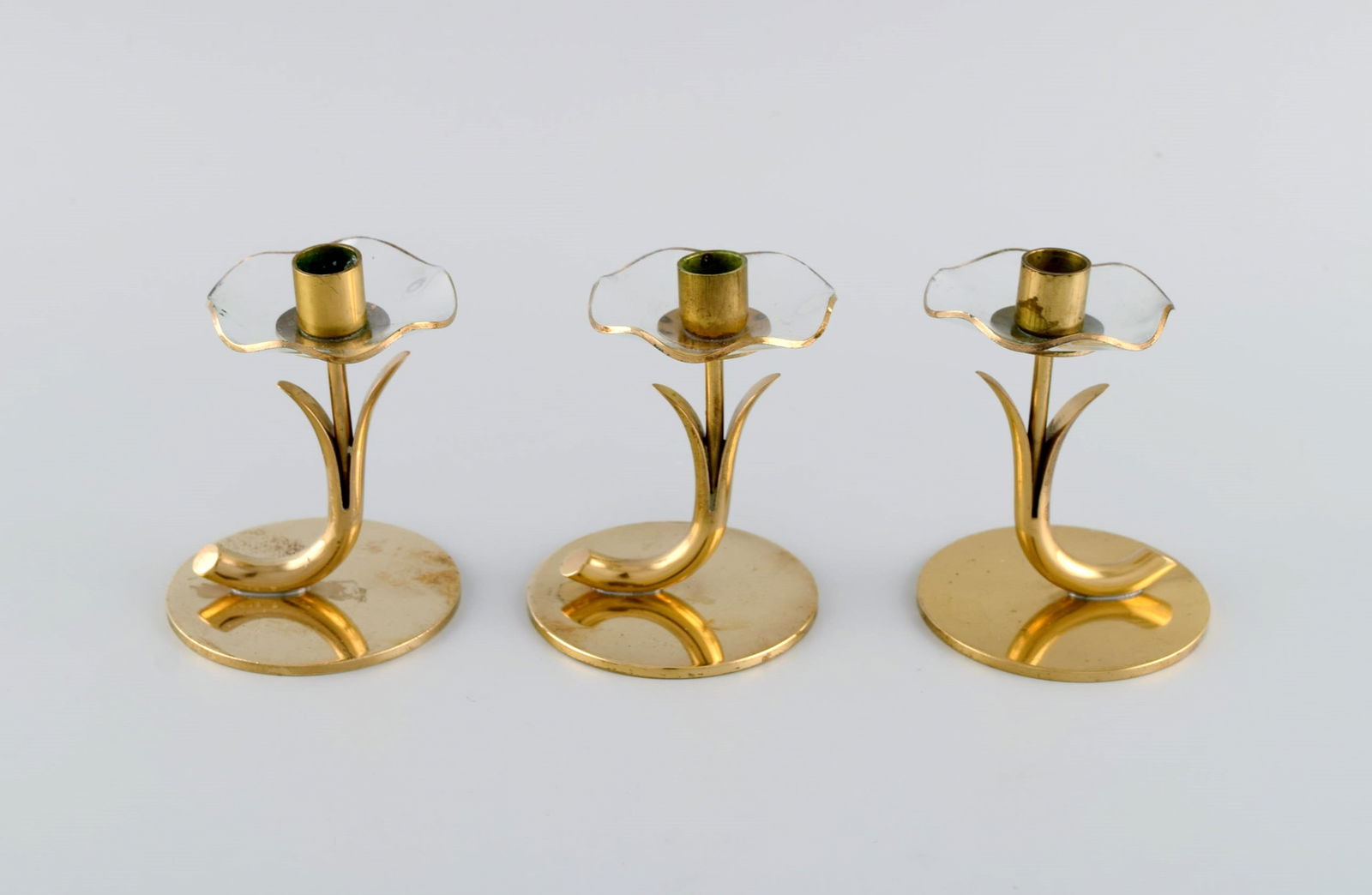 Gunnar Ander for Ystad Metall. Three candlesticks in brass and clear art glass shaped like flowers.: Gunnar Ander for Ystad Metall. Three candlesticks in brass and clear art glass shaped like flowers. 1950s. Measures: 8.5 x 6.5 cm. In excellent condition. Stamped. Reserve: $210.00 Shipping: Domestic:
