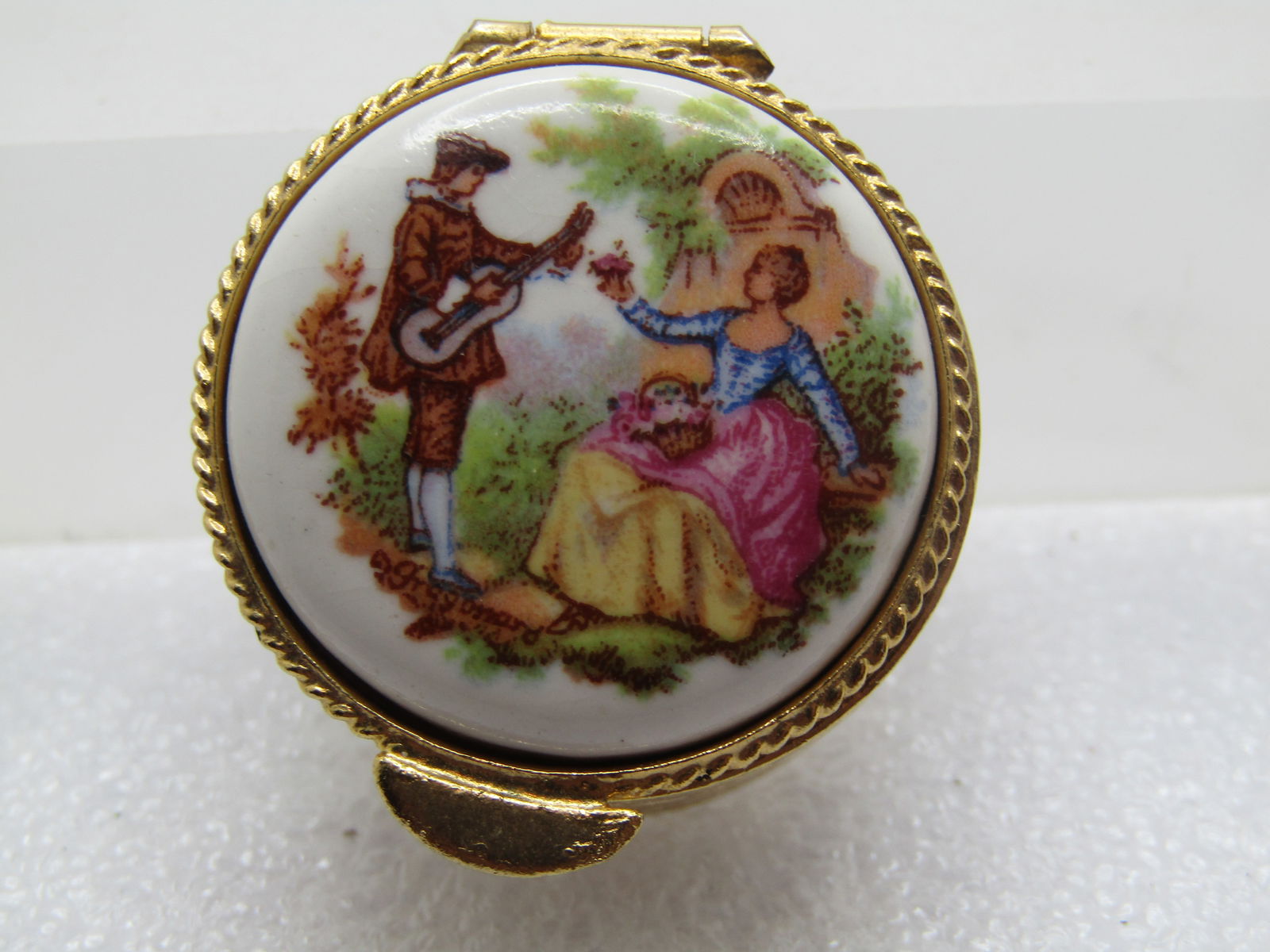 Vintage French Courting Scene Pill Box, 1960's-1970's: Vintage French Courting Scene Pill Box, 1960's-1970's. Gold tone with a scrolled design around the sides of the round pillbox with a courting scene on top on a ceramic domed on the sides and flat on t