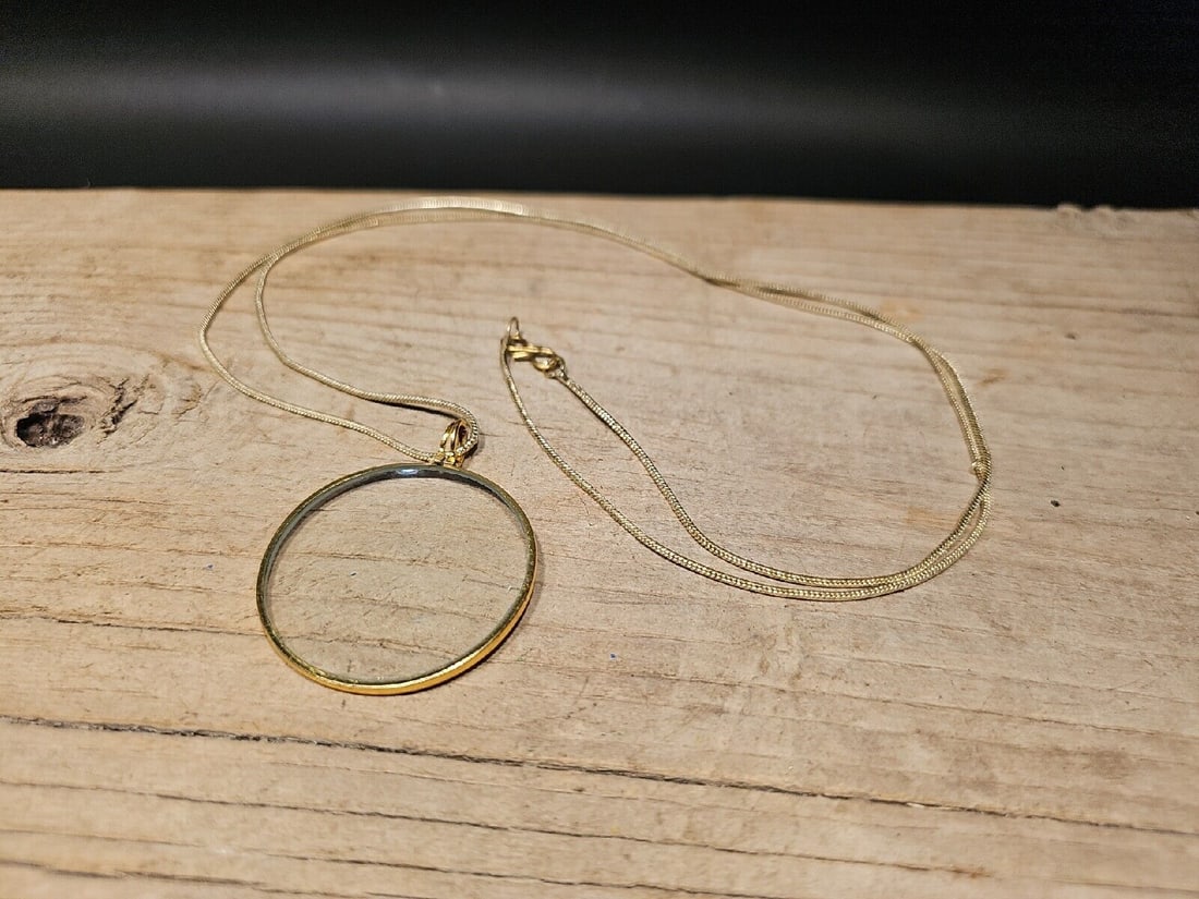 1 3/4" Brass Magnifying Glass Necklace: 1-3/4" 20" hanging height 37" long chain The 1-3/4" Magnifying Glass on Necklace is a captivating antique reproduction piece that combines elegance and functionality in a single accessory. This intric