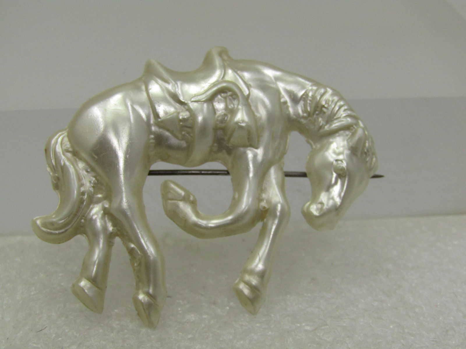 Vintage Celluloid Horse/Bucking Bronco Brooch, 1940's: Vintage Celluloid Horse/Bucking Bronco Brooch, 1940's. Pearly white with a saddle and horse in a bucking pose. It is appx. 2" by 1.75. Plastic c-clasp. Very good condition. Great for rodeo and equine