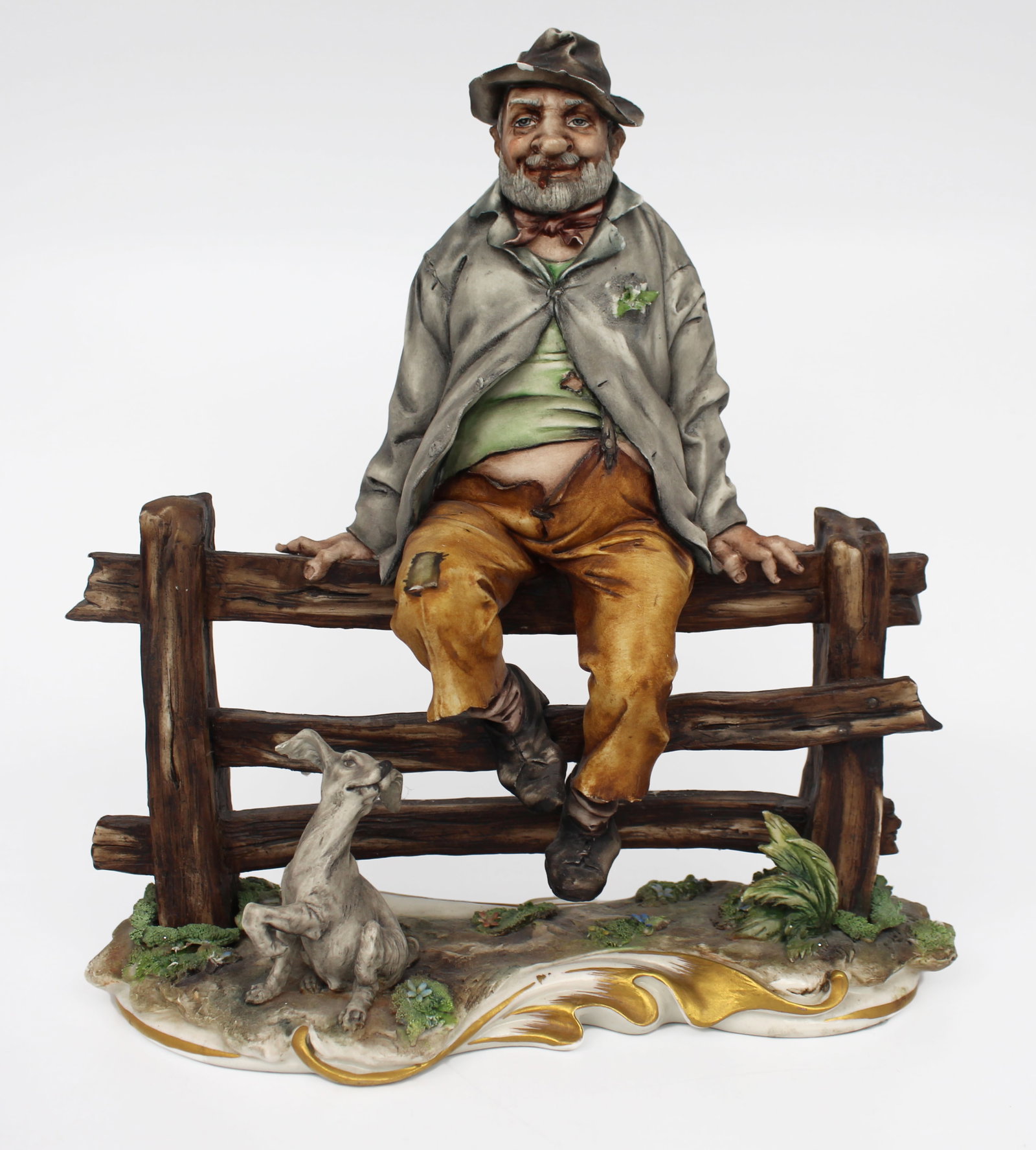 Capodimonte Tramp on Fence: Capodimonte Tramp on Fence Made in Italy, c.1970. Finely modelled with lots of detail, hand painted. Capodimonte Tramp on Fence. Blue factory stamp to the underside Measures 25 x 11 x 27 (height) cm.