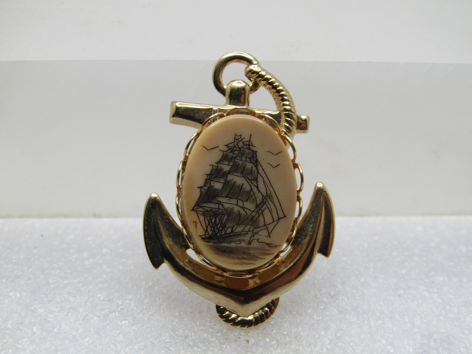 Vintage Sail Ship Scrimshaw Anchor Brooch, 1960's-1970's: Vintage Scrimshaw Anchor Brooch, 1960's-1970's. Gold tone with a3/4: by 1/2: oval tall ship scrimshaw piece set in a scalloped bezel and set over a gold tone pressed metal anchor base. The brooch is a