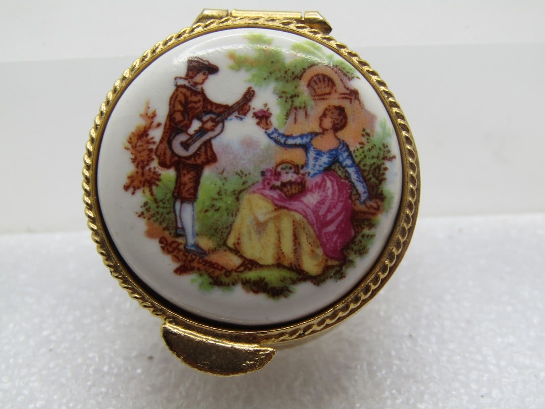 Vintage French Courting Scene Pill Box, 1960's-1970's: Vintage French Courting Scene Pill Box, 1960's-1970's. Gold tone with a scrolled design around the sides of the round pillbox with a courting scene on top on a ceramic domed on the sides and flat on t