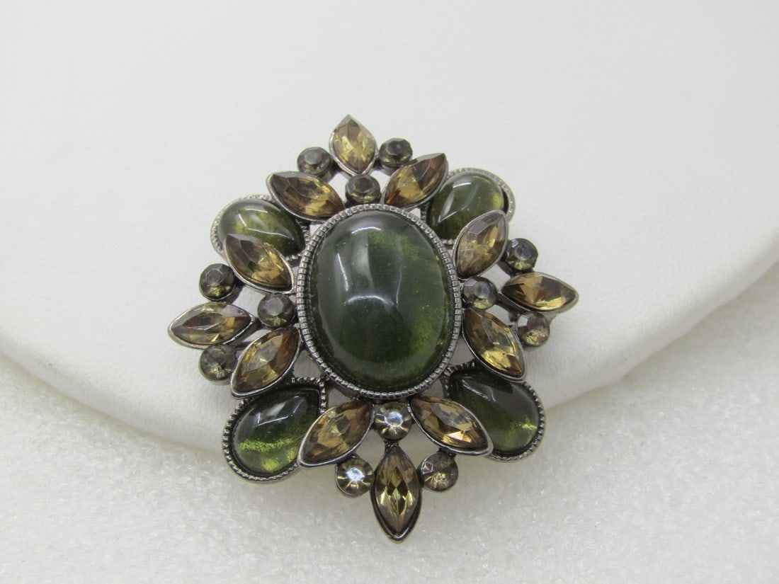 Vintage Monet Rhinestone Brooch, Black Metal, 2" Green and Brown: Vintage Monet Rhinestone Brooch, Black Metal, 2" by 1.5" Green and Brown acrylic stones. 1980's-1990's. Oval green 18mm by 13.5mm in the center with smaller ovals in the same color on the corners, ang
