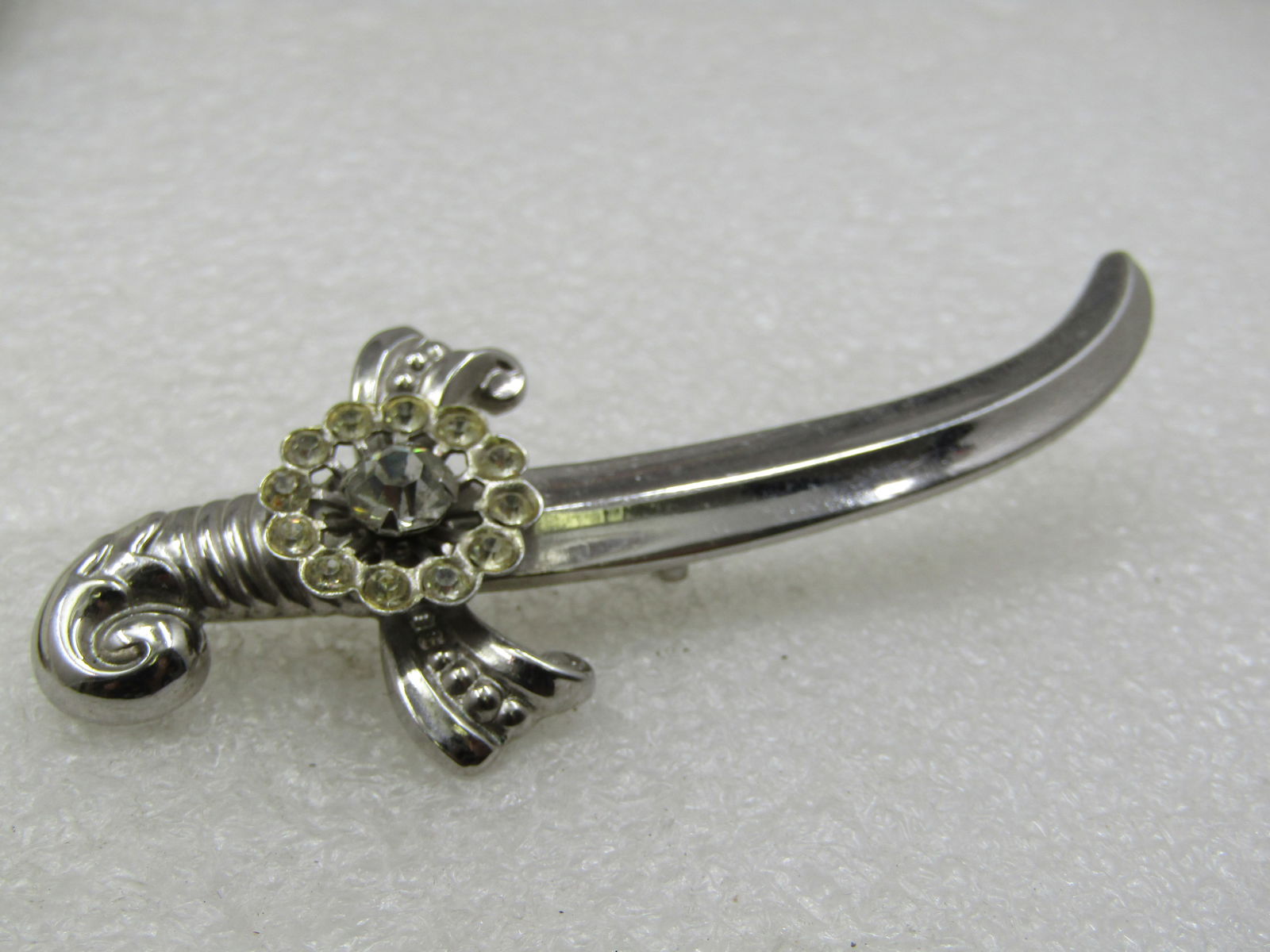 Vintage Coro Rhinestone Sword Brooch, 3.25", 1940's: Vintage Coro Rhinestone Sword Brooch, 3.25" by 1.25", 1940's. Silver tone. There is a rhinestone center 6mm stone at the hilt with a halo of smaller clear rhinestones around it. Decorative grip on the