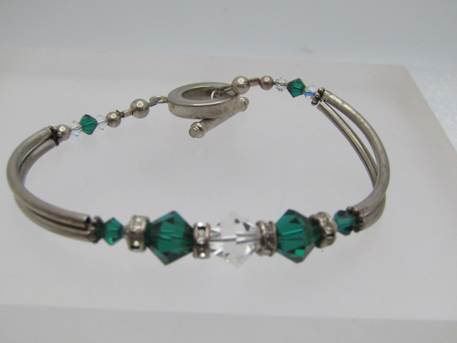 Vintage Emerald & Clear Crystal Bracelet, Toggle, 7.5", 1980's-1990's: Vintage Emerald & Clear Crystal Bracelet, Toggle, 7.5", 1980's-1990's. This has two curved silver tone bar sections and across the top of the ring are rhinestone rondelle links and well as faceted eme