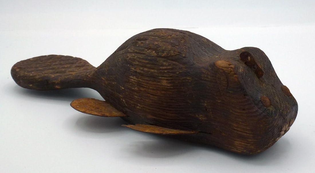 A rare fishing lure in the form of a beaver: This is a fishing lure in the form of a beaver. It has a wood body with carved detail on the tail, ears, and teeth, metal tacks for eyes, and sheet metal legs. An arrow shaped cavity was carved in the