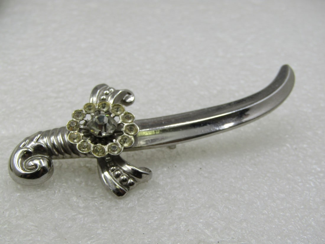 Vintage Coro Rhinestone Sword Brooch, 3.25", 1940's: Title:Vintage Coro Rhinestone Sword Brooch, 3.25", 1940's Description:Vintage Coro Rhinestone Sword Brooch, 3.25" by 1.25", 1940's. Silver tone. There is a rhinestone center 6mm stone at the hilt with