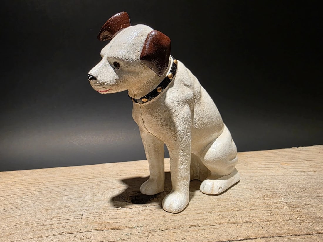 Cast Iron Nipper Dog Coin Bank: 6 L x 2 W x 6 H Wonderful reproduction vintage-style coin bank, hand-painted in white with brown ears and a black collar. The statue is made of cast iron, giving it a heavy and durable feel. It measur