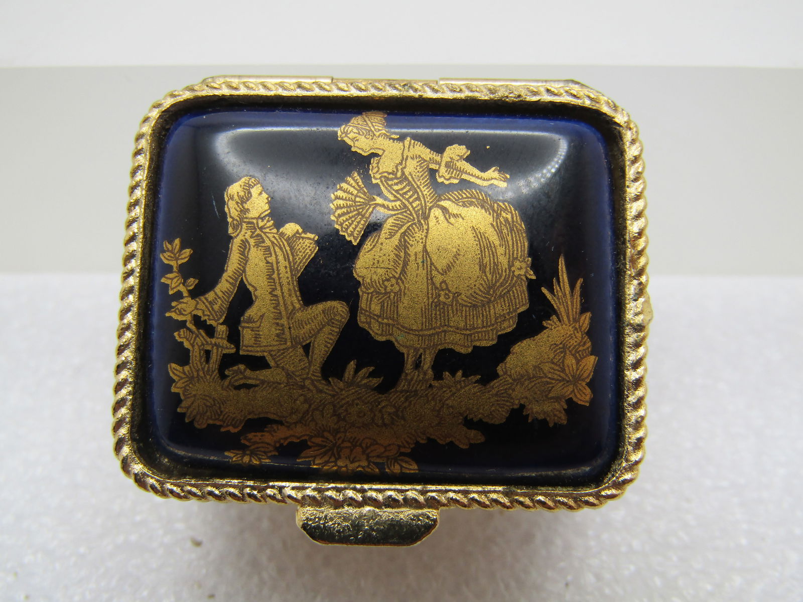 Vintage Courting Scene Pill Box, 1960's-1970's: Vintage Courting Scene Pill Box, 1960's-1970's. Dark blue background, slightly domed from the edges with a gold French courting scene in gold. It is rectangular a appx. 1.25" wide and 1-1.8" front-to-