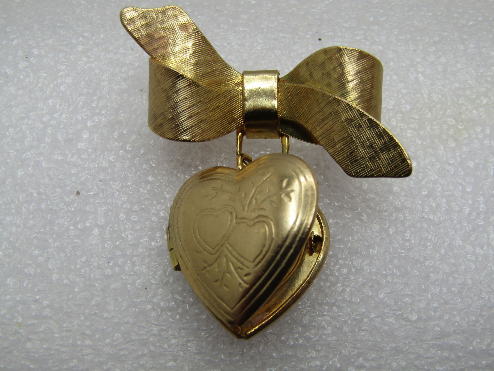 Vintage Bow & Heart Locket Brooch, 1960's: Vintage Bow & Heart Locket Brooch, 1960's. This has a textured and smooth finished bow on top with a dangle heart locket with two hearts on the face of the locket. The brooch is gold tone and appx. 1.