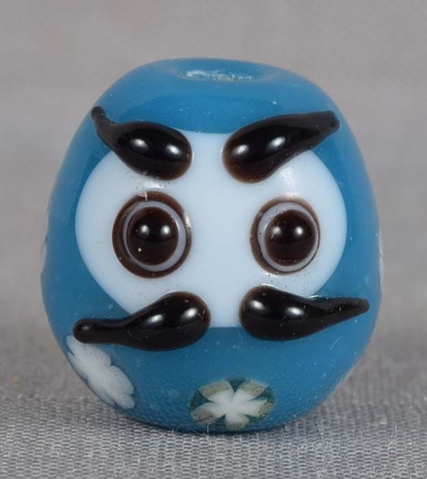 Japanese glass OJIME tombodama DARUMA in flower robe: Japanese glass ojime in a form of tombodama bead representing Zen Buddhism Patriarch Daruma enveloped in blue robe with various flowers. Tombodama can be translated as Òdragonfly ballÓ and the name