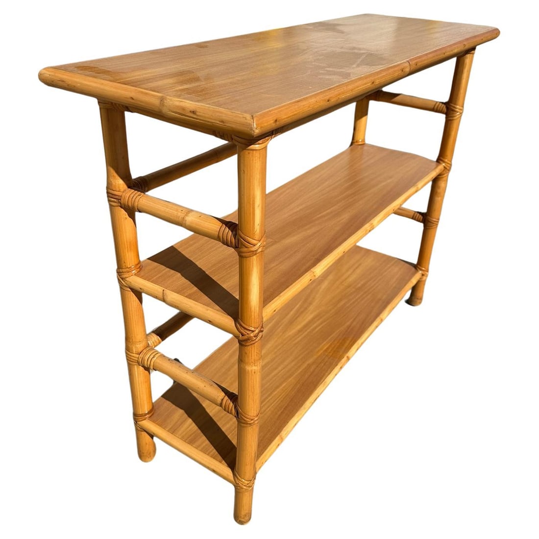 Post War Restored Mid-Century Rattan and Mahogany Bookcase Console Table: Postwar three-tier console table Bookshelf with mahogany tops and a wrapped stick rattan frame. The table has mahogany tops along each shelf which are decorated with rattan trim and each shelf has rat