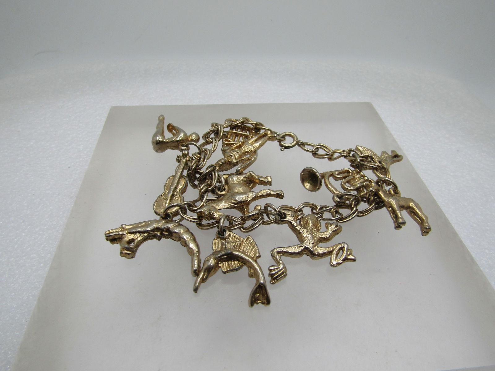 Vintage Gold Tone Charm Bracelet, 1960's. 11 Charms, 7": Vintage Gold Tone Charm Bracelet, 1960's. 11 Charms, 7". A bird (heron?); donkey' French horn; frog; marlin; shrimp; horse; knight; Indian Chief; violin; swimmer; musical bar with rhinestone (one miss