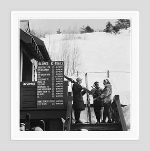 Slim Aarons 'Three Skiers' 1955 White Frame Silver Gelatine Resin Print: Description Slim Aarons 'Three Skiers' 1955 White Frame Silver Gelatine Resin Print Three skiers in New Hampshire, 1955. A sign near them lists the local slopes and trails. (Photo by Slim Aarons) 