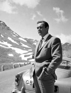 James Bond 007 White Framed: Description James Bond 007 Sean Connery next to the infamous 007 silver Aston Martin DB5 car on a mountainous road in James Bond film ‘Goldfinger’, directed by Guy Hamilton, 1964. 