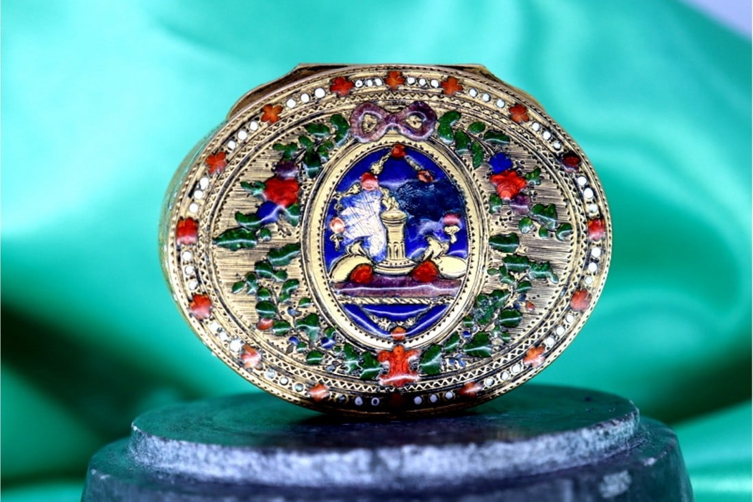 ELLIPTICAL GOLD PILL BOX WITH ENAMEL RELIEFS, ENGRAVED FLORAL MOTIFS AND FRIEZES WITH BANDS ALONG: Title: ELLIPTICAL GOLD PILL BOX WITH ENAMEL RELIEFS, ENGRAVED FLORAL MOTIFS AND FRIEZES WITH BANDS ALONG THE LENGTH INVOLVING NATURAL AND MUSICAL ELEMENTS Description: Elliptical gold pill box with en