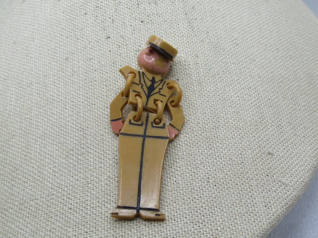 Vintage Celluloid WWII US Army Soldier Brooch, Articulated, 1940's: Vintage Celluloid WWII US Army Soldier Brooch, Articulated, 1940's. Olive drab uniform with tie and black lines for details with a cap with black bring. It has dangling arms and legs. One eye is raise