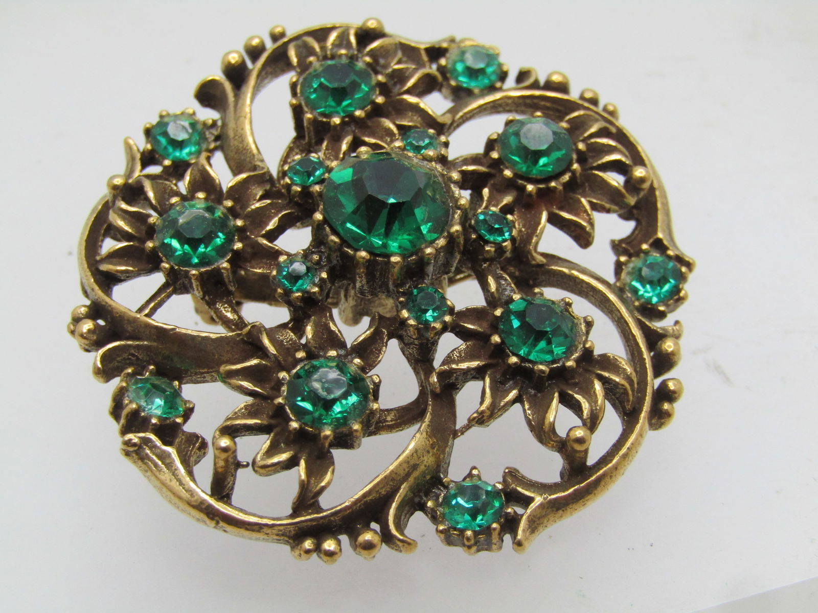 Vintage Green Rhinestone Spiral Blossom Brooch, Signed Coro 1960's: Vintage Green Rhinestone Spiral Blossom Brooch, Signed Coro 1960's. Brassy gold tone with blossoms and a raised center emerald green rhinestones that is appx. 8.5mm top center and 4.5mm in the center