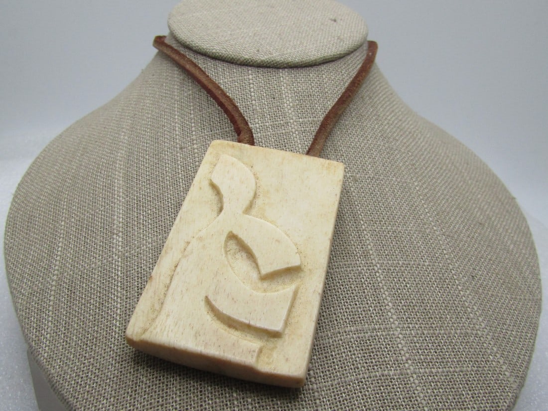 Vintage Carved Bone Necklace, Leather 24", 1970's-1980's, Unisex: Vintage Carved Bone Necklace, Leather 24", 1970's-1980's, Unisex. 1.75" tall and 1.7" wide rectangular carved bone with a symbol on top. The necklace is made of 3mm square brown leather that is set on