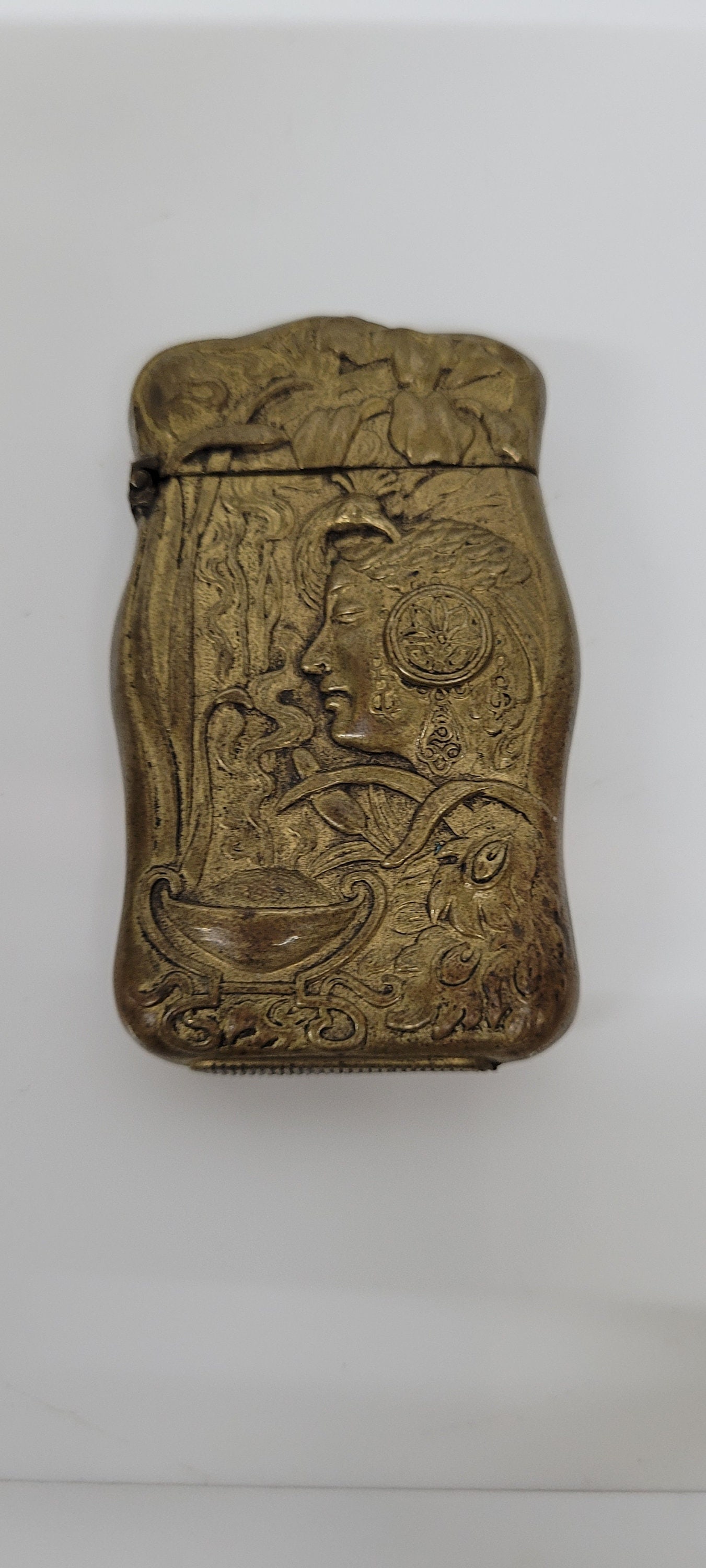 A gold metal matchbox with an ornate design featuring a woman's face and floral motifs.: Vintage from the 19th century Materials: metal, brass The hinge is in good condition and works great. The safe its self is in great shape. Minor wear, scratches and tarnish. This match safe is a gem,