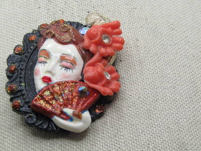 Vintage Woman With Fan & Flowers Brooch, Porcelain, 1960's-1970's: Vintage Woman With Fan & Flowers Brooch, Porcelain, 1960's-1970's. This is a layered design with a black scalloped bse with orange glitter and a porcelain woman's head with brown hair, closed eyes, re