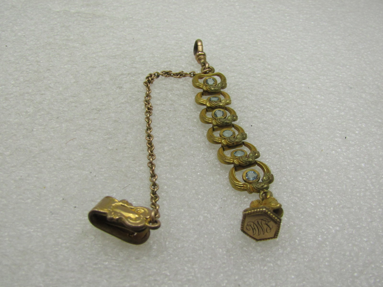 Victorian 12kt G.F. Watch Chain With Stones, Engraved SMA, Floral Accent 8": Victorian 12kt G.F. Watch Chain With Stones, Engraved SMA, Floral Accent 8". Age is lae 1800's. Six links with curved open design and center blue rhinestone. At the end is a fob with the initial engra